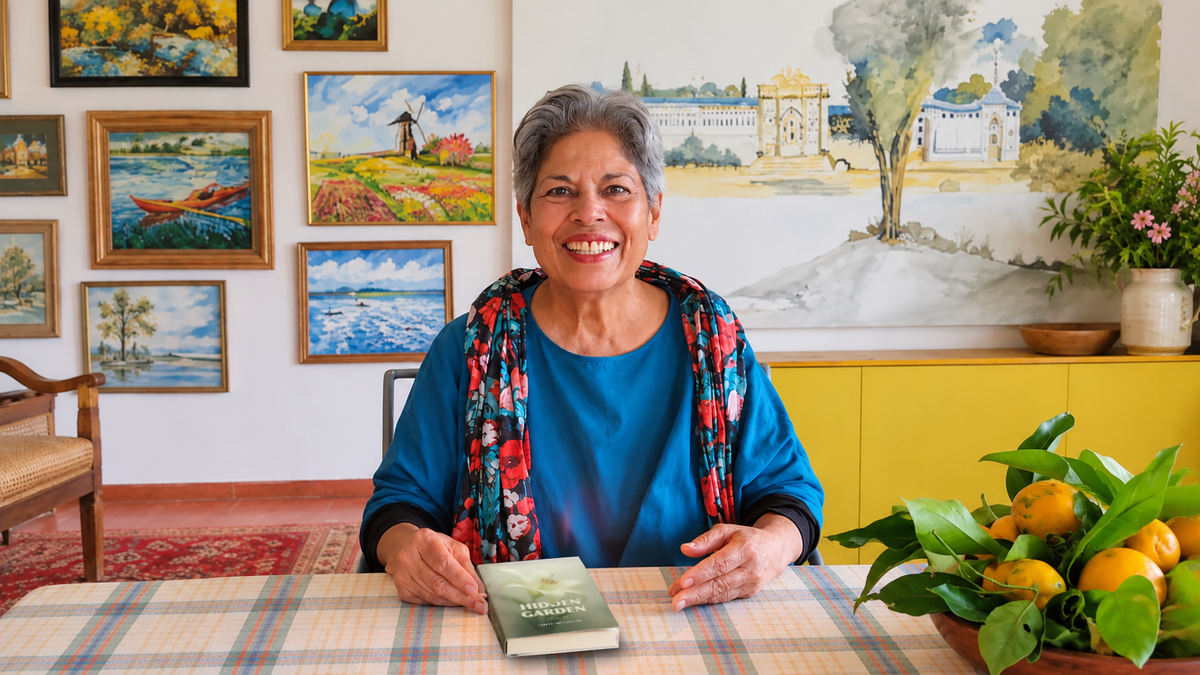 Tanya Mendonsa, poet, writer and painter, sits smiling at a table, holding a book titled 'Hidden Garden' in front of her. She is wearing a blue top and a coluorful floral scarf.